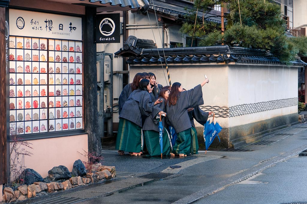 girls in yukatas pose on the street at kinosaki onsen